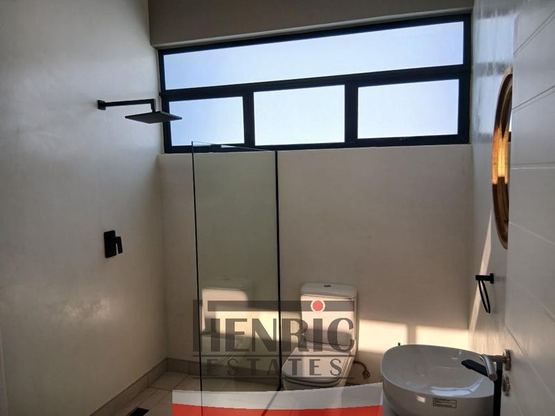 Modern bathroom featuring a walk-in shower with black fixtures, a sleek basin, and a toilet, finished with clean tiling and natural light.