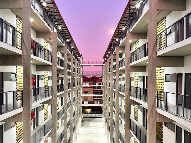 A symmetrical view of a modern apartment complex featuring multiple levels of balconies with metal railings and concrete structural pillars.