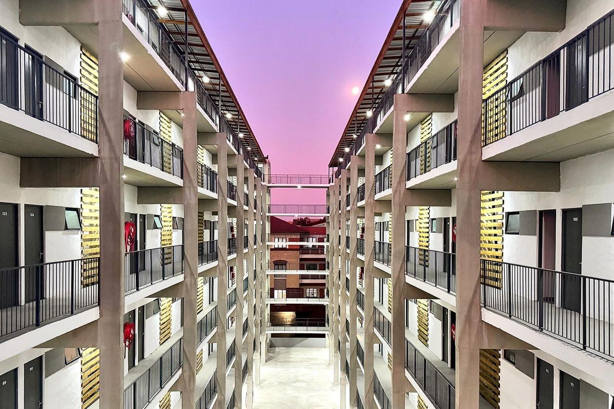 A symmetrical view of a modern apartment complex featuring multiple levels of balconies with metal railings and concrete structural pillars.