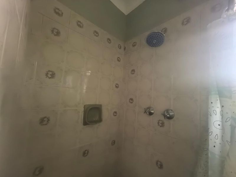 A dated shower enclosure featuring patterned ceramic wall tiles, a fixed shower head, and a recessed soap dish.