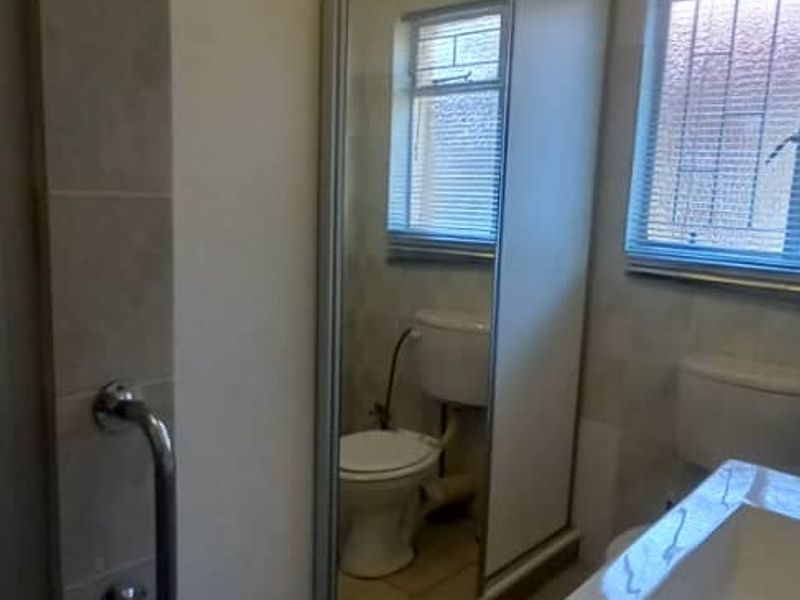 A functional bathroom featuring a vanity, toilet, and large mirror-fronted storage cupboard, finished with ceramic floor tiles and security-barred windows.
