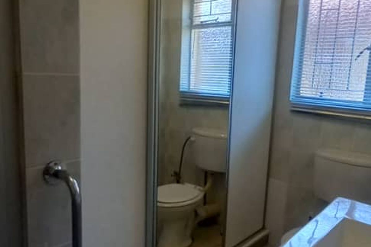 A functional bathroom featuring a vanity, toilet, and large mirror-fronted storage cupboard, finished with ceramic floor tiles and security-barred windows.