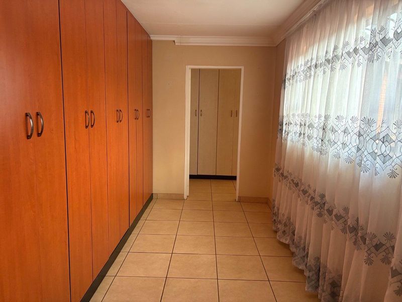 A functional hallway featuring extensive built-in wooden cabinetry, tiled flooring, and natural light through a large window.