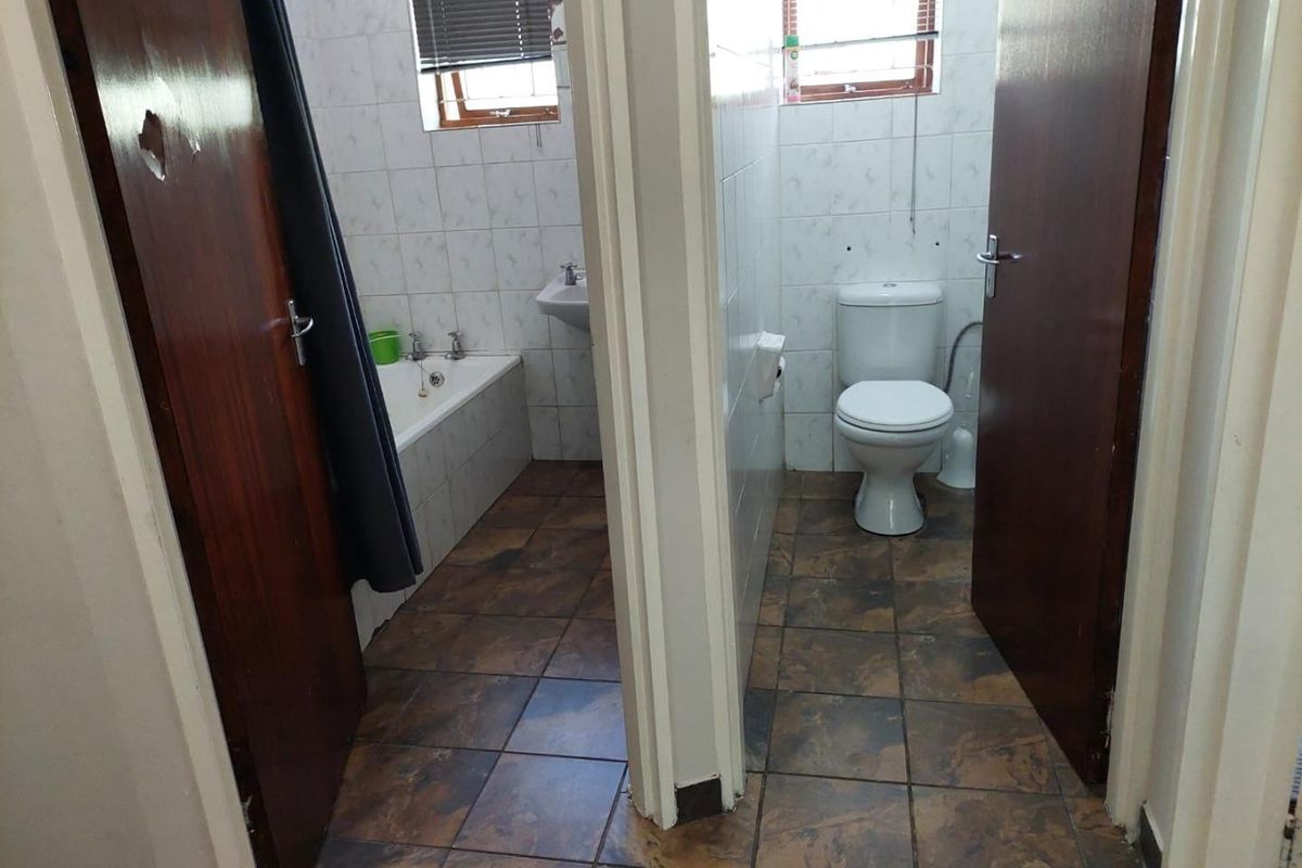 A functional bathroom featuring a separate bathtub area and toilet, finished with tiled flooring and wall tiles, requiring cosmetic updates.