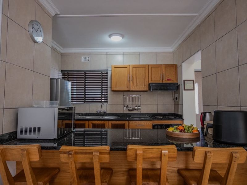 A functional kitchen featuring granite countertops, wooden cabinetry, a built-in hob with extractor fan, and a convenient breakfast bar for casual dining.