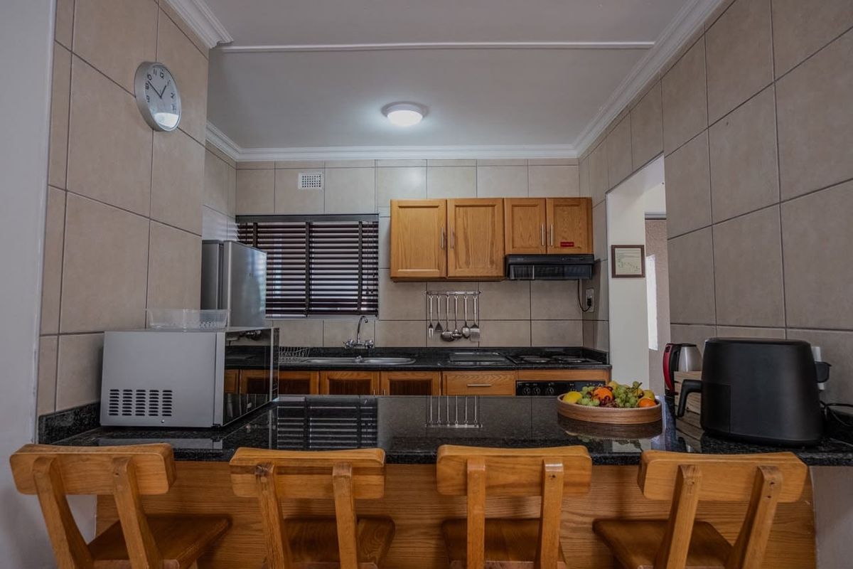 A functional kitchen featuring granite countertops, wooden cabinetry, a built-in hob with extractor fan, and a convenient breakfast bar for casual dining.