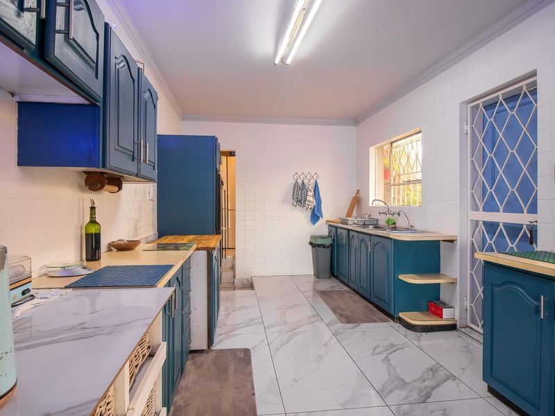 A functional kitchen featuring blue built-in cabinetry, marble-look tiled flooring, tiled walls, and a double sink with direct access to an exterior security gate.