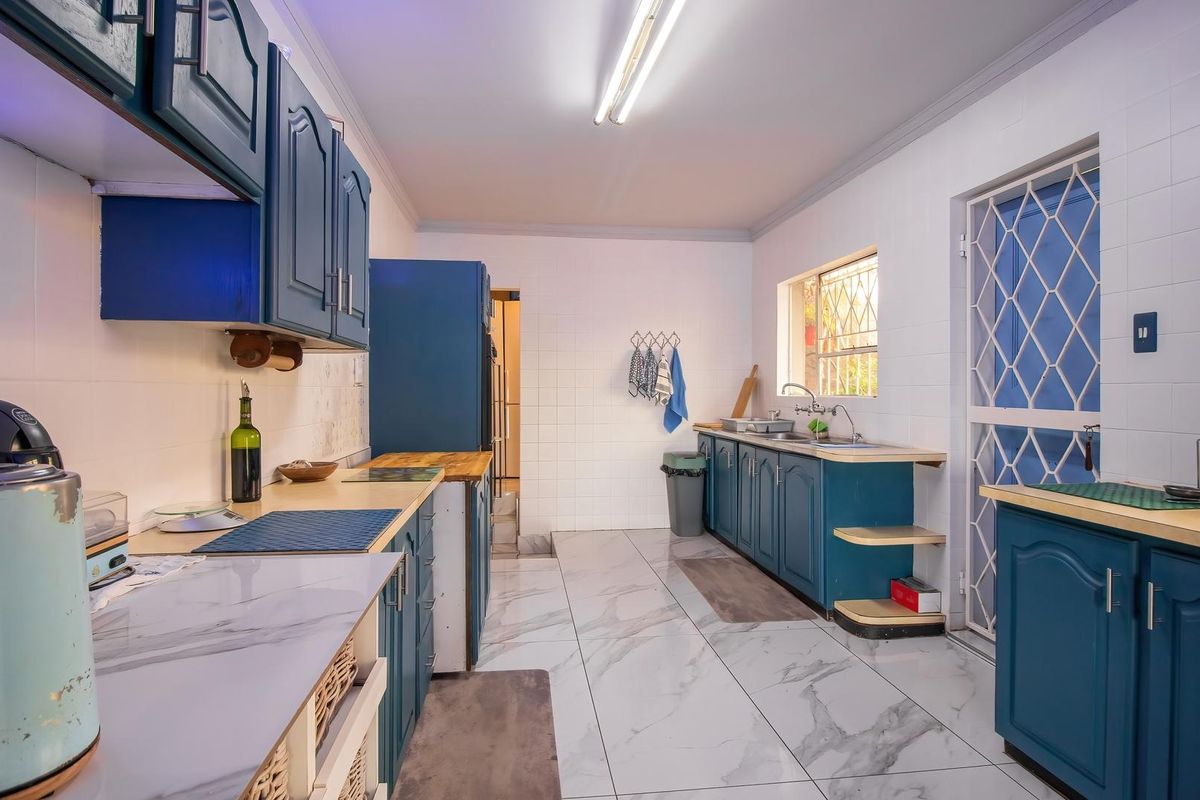 A functional kitchen featuring blue built-in cabinetry, marble-look tiled flooring, tiled walls, and a double sink with direct access to an exterior security gate.