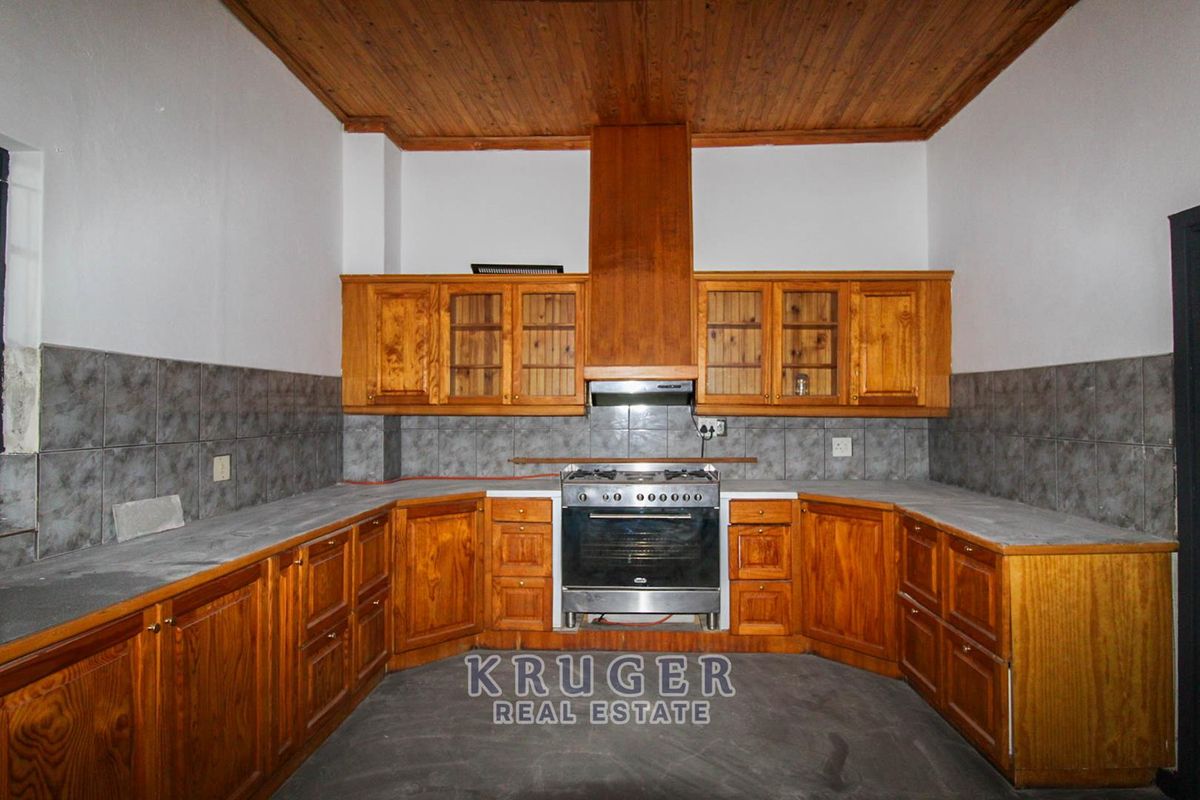 A dated kitchen featuring wooden cabinetry, a freestanding stove with extractor fan, tiled backsplash, and a wooden ceiling.