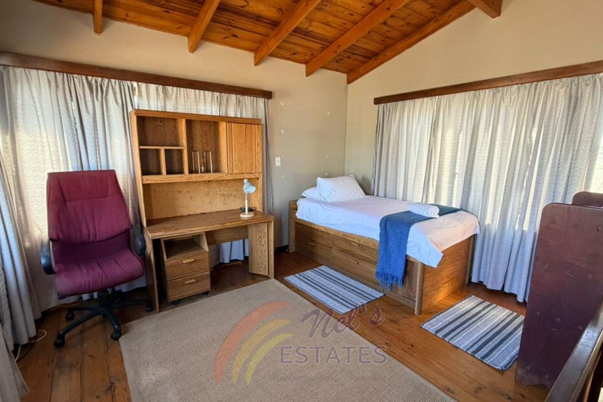 A bedroom featuring exposed timber ceiling beams and wooden flooring, providing a rustic aesthetic with natural light through large windows.