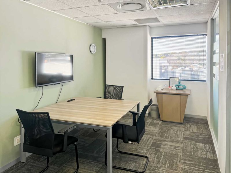 A functional office space featuring carpet tiles, a suspended ceiling with recessed lighting, and a glass partition wall, providing a professional work environment.