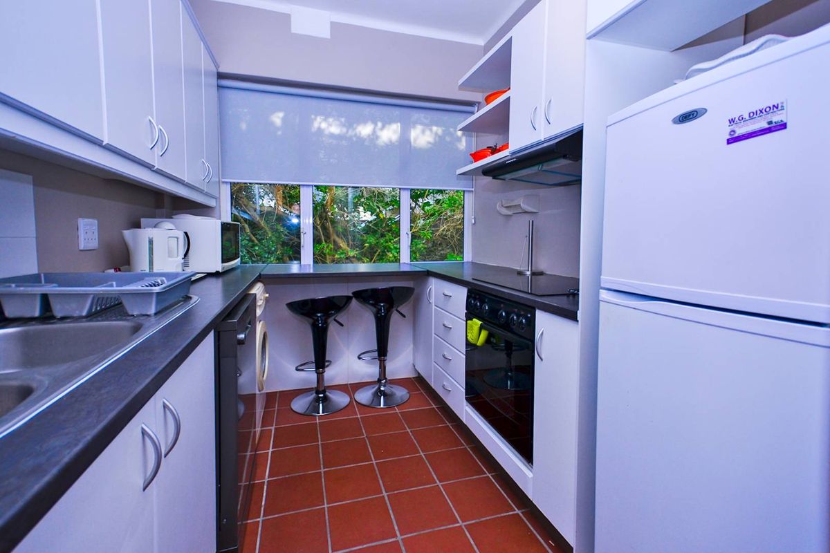 Compact kitchen featuring white cabinetry, dark countertops, built-in oven with hob, and tiled flooring with a breakfast bar area.