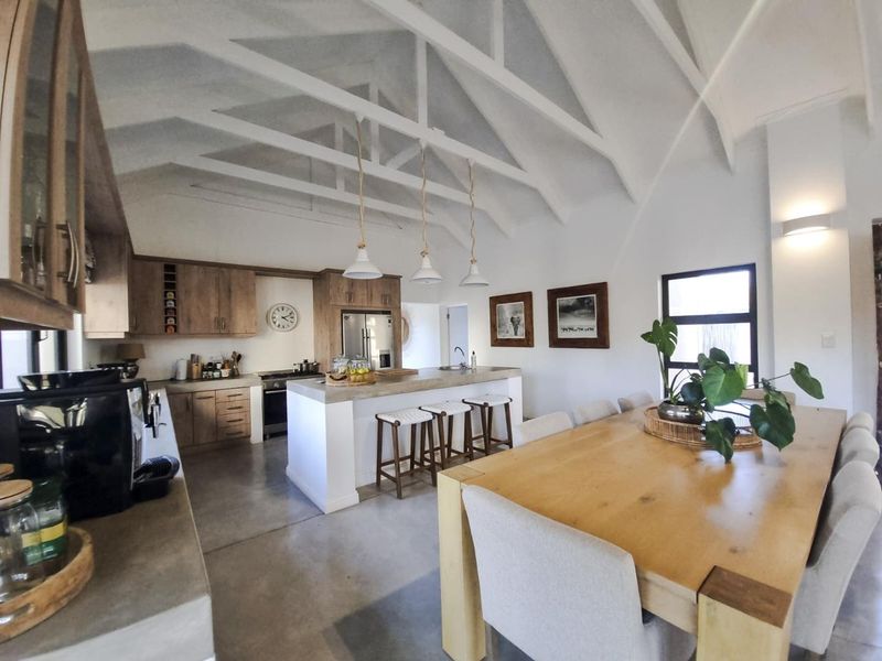 Spacious open-plan kitchen and dining area featuring high vaulted ceilings with exposed trusses, polished concrete floors, and a modern kitchen island.
