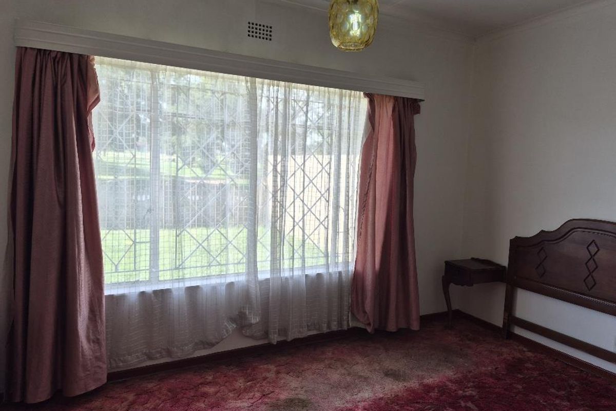 A bedroom featuring a large window with security bars, a built-in curtain pelmet, and carpeted flooring.