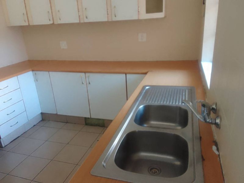 A functional kitchen area featuring laminate countertops, a double bowl stainless steel sink, and built-in cabinetry with ceramic floor tiling.