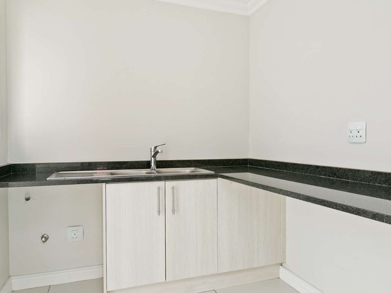 A clean and functional laundry area featuring granite countertops, a stainless steel sink, and built-in cabinetry with dedicated plumbing connections.