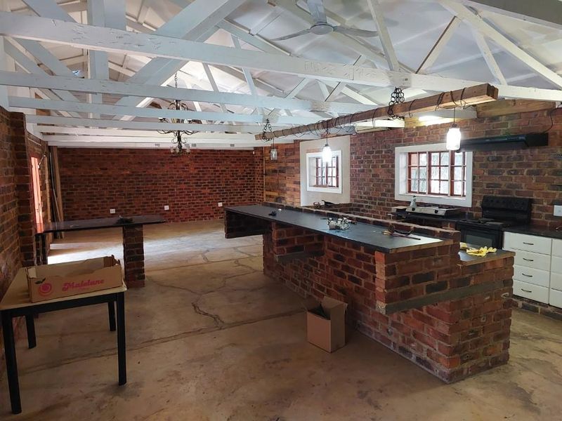 Spacious open-plan living and kitchen area featuring rustic exposed brick walls, timber rafters, and a large brick-built kitchen island with integrated appliances.