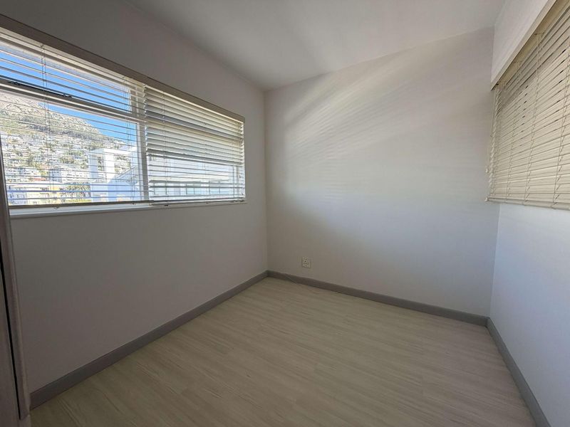A bright, empty bedroom featuring light-toned laminate flooring, neutral walls, and venetian blinds, offering a clean canvas for personalization.