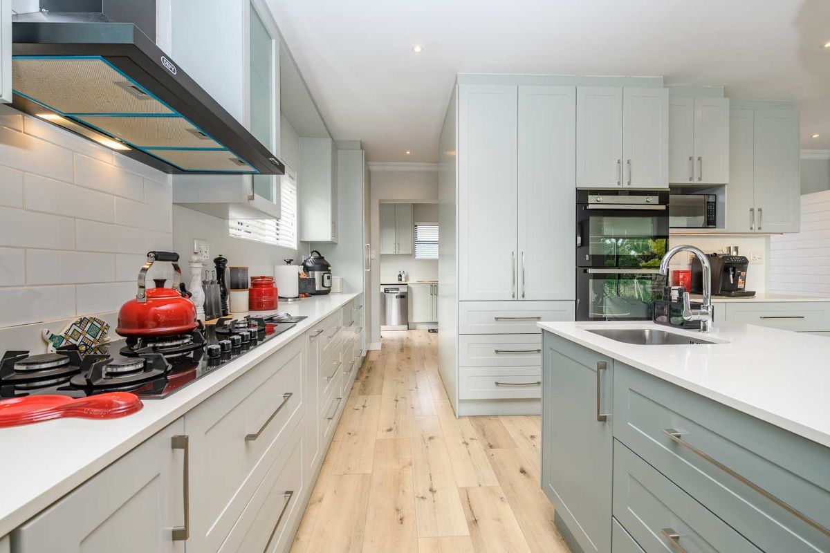 Modern kitchen featuring light-toned cabinetry, stone countertops, a gas hob with extractor fan, built-in double oven, and a central island with a sink.