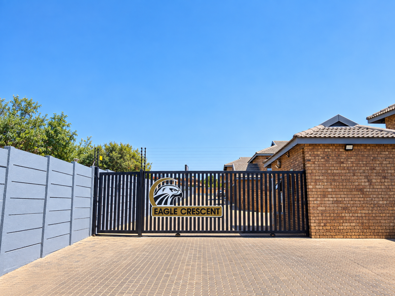 The secure entrance to Eagle Crescent townhouse complex, featuring a modern sliding gate, brick perimeter walling, and a well-maintained paved driveway.