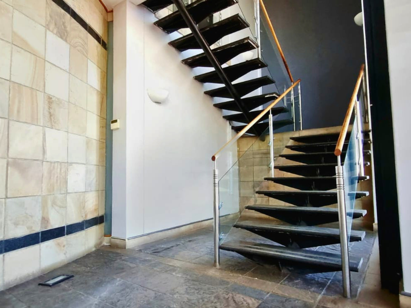 Modern entrance foyer featuring an open-tread staircase with glass balustrades, stone wall cladding, and durable stone floor tiles.