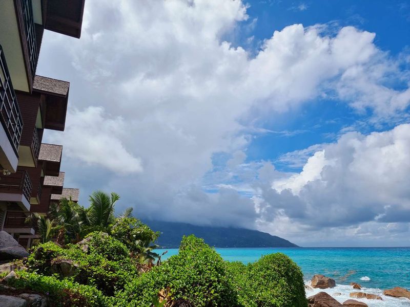 A scenic view of the coastline featuring lush tropical landscaping, rocky outcrops, and the multi-story building facade overlooking the ocean.