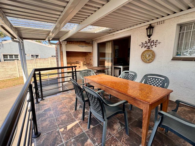 Covered patio area featuring a built-in braai, tiled flooring, and metal railing, providing a functional outdoor entertainment space.
