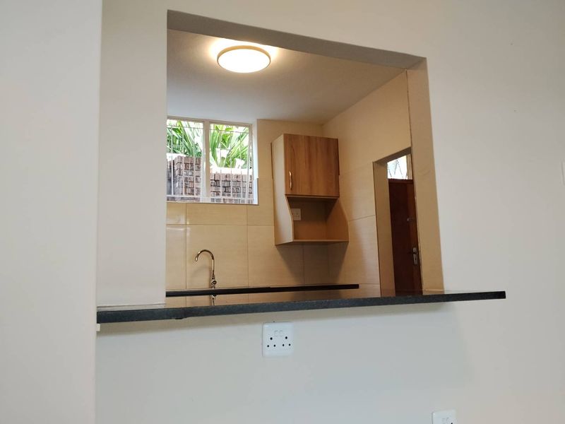A clean, functional kitchen area featuring built-in cabinetry, a dark granite countertop, and a tiled backsplash, viewed through a convenient serving hatch.