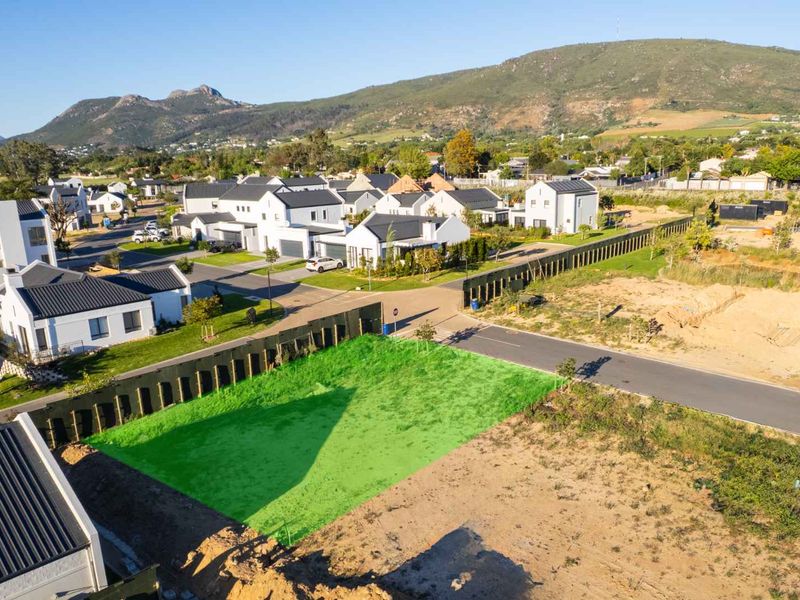 Aerial view of a vacant residential plot in a developed estate, featuring surrounding infrastructure and mountain views.
