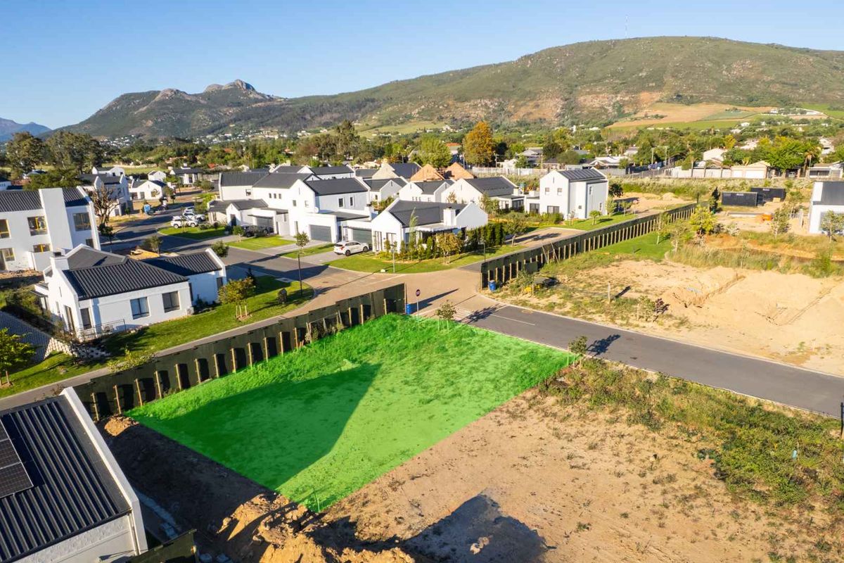 Aerial view of a vacant residential plot in a developed estate, featuring surrounding infrastructure and mountain views.