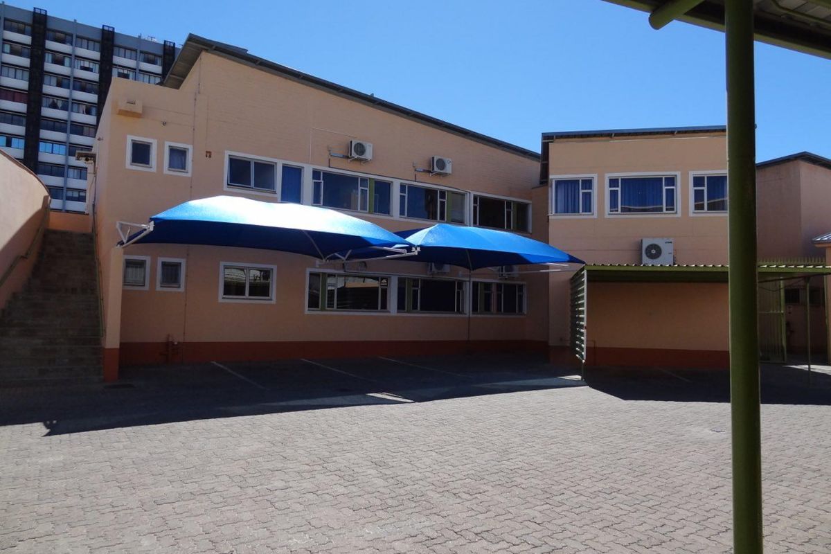 Exterior view of the office building featuring a paved parking area with blue shade sails and multiple wall-mounted air conditioning units.