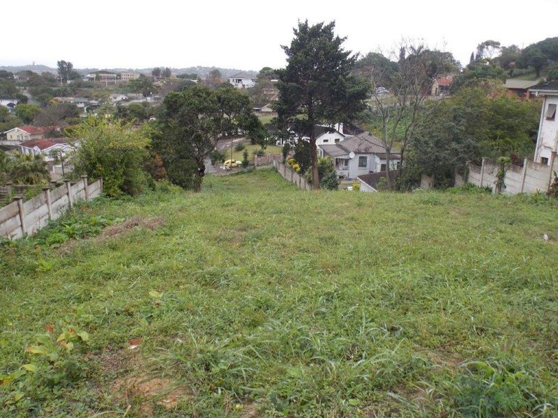 A view overlooking a sloped residential plot of land with established boundary walls and surrounding neighborhood scenery.