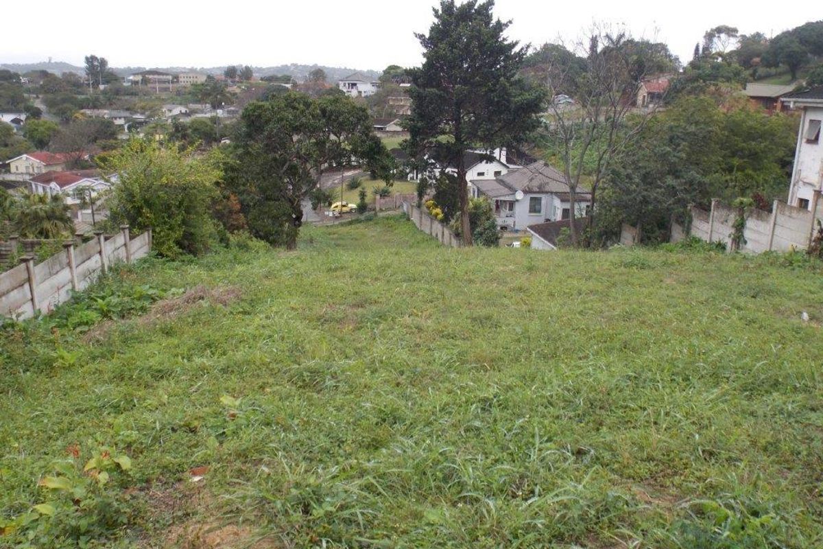 A view overlooking a sloped residential plot of land with established boundary walls and surrounding neighborhood scenery.