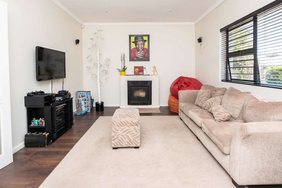 A comfortable living room featuring a built-in fireplace, dark laminate flooring, and large windows with venetian blinds, offering a cozy and functional space.
