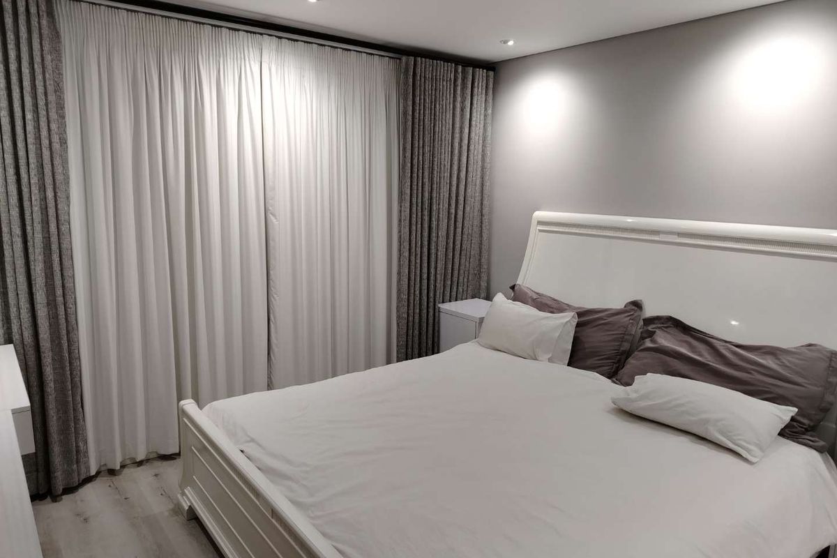 A well-maintained bedroom featuring recessed ceiling lighting, light-toned wood-look flooring, and floor-to-ceiling curtains.