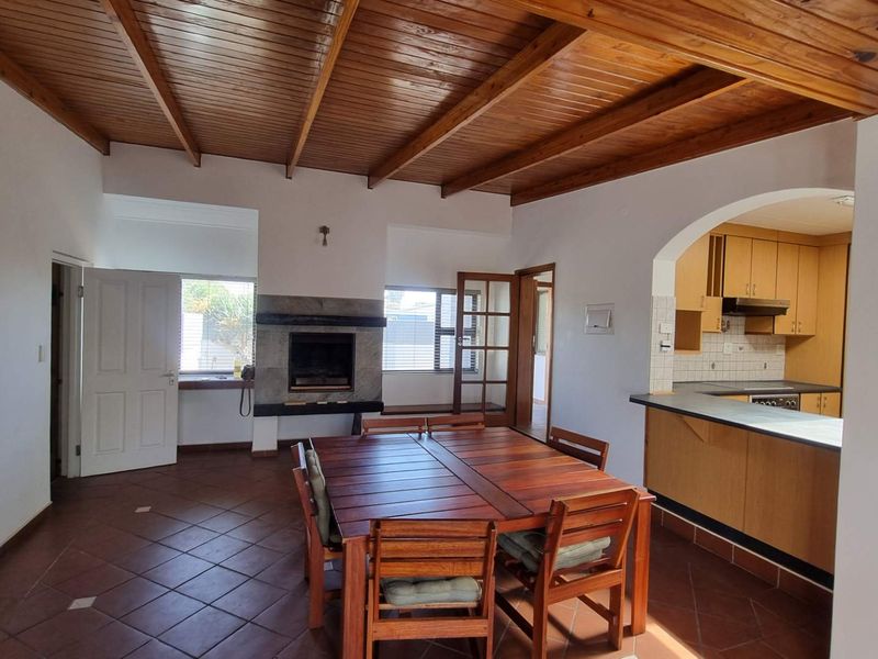Open plan living and dining area featuring a built-in fireplace, exposed timber ceiling, and an adjoining kitchen with wooden cabinetry.