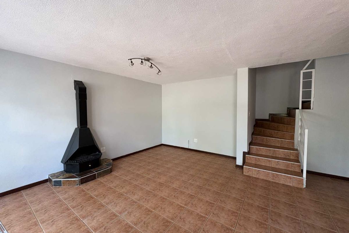 An open-plan living area featuring tiled flooring, a built-in fireplace, and a staircase leading to the upper level.