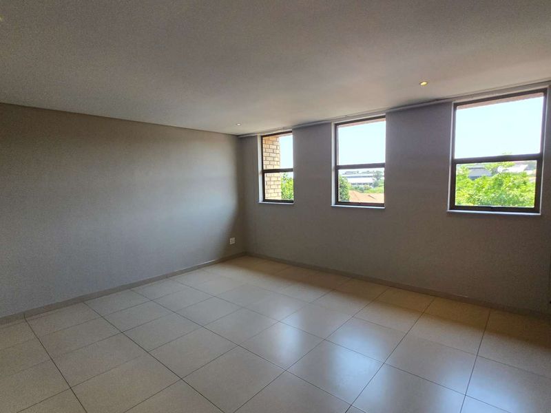 Spacious open-plan living area featuring modern tiled flooring, recessed downlights, and a characterful exposed brick feature wall with large windows.