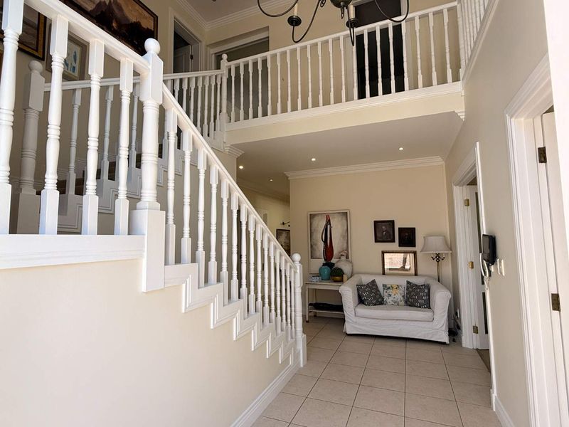 Spacious double-volume entrance hall featuring a classic staircase with white balustrades, tiled flooring, and elegant coving.