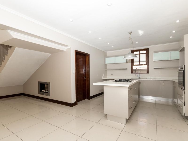 Modern kitchen featuring a central island with gas hob, built-in oven, sleek cabinetry, and tiled flooring, adjacent to a staircase with a built-in fireplace.