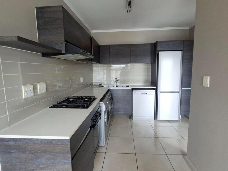 Modern kitchen featuring dark wood-look cabinetry, stone countertops, gas hob, extractor fan, and tiled flooring in a clean, well-maintained apartment setting.