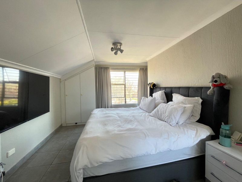 A bedroom featuring tiled flooring, a sloped ceiling, and built-in cupboards, with a window providing natural light.