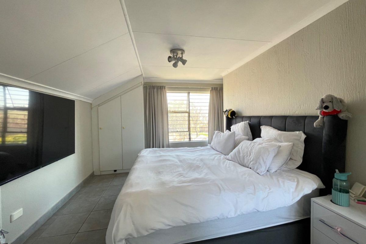 A bedroom featuring tiled flooring, a sloped ceiling, and built-in cupboards, with a window providing natural light.