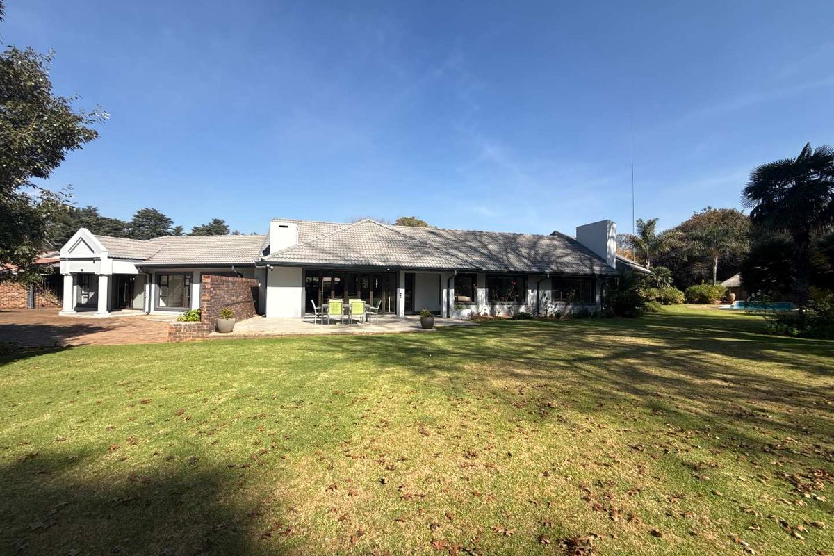 A spacious rear view of the house featuring a large manicured lawn, paved patio area, and tiled roof structure.