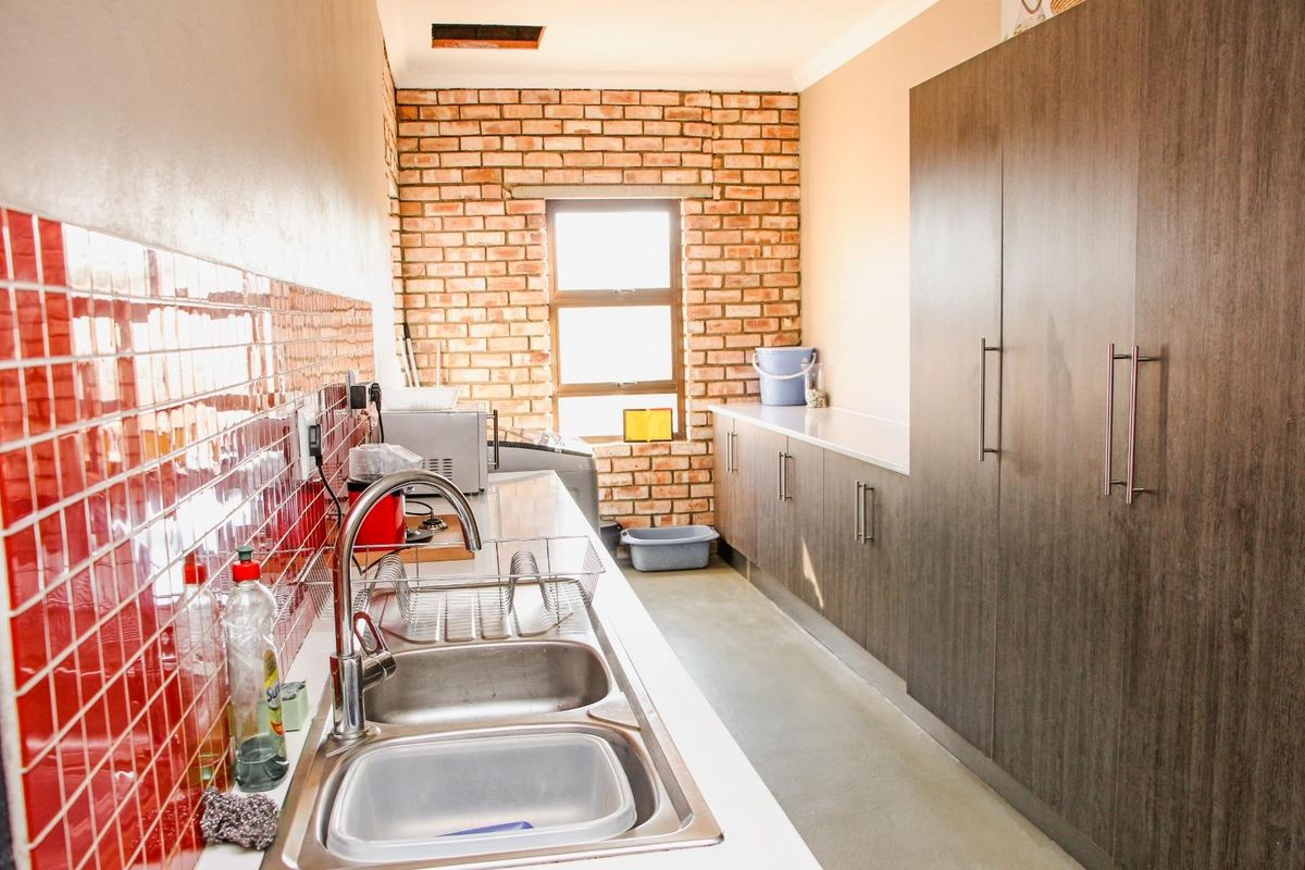 A functional scullery featuring a double stainless steel sink, ample built-in cabinetry, and an exposed brick feature wall.