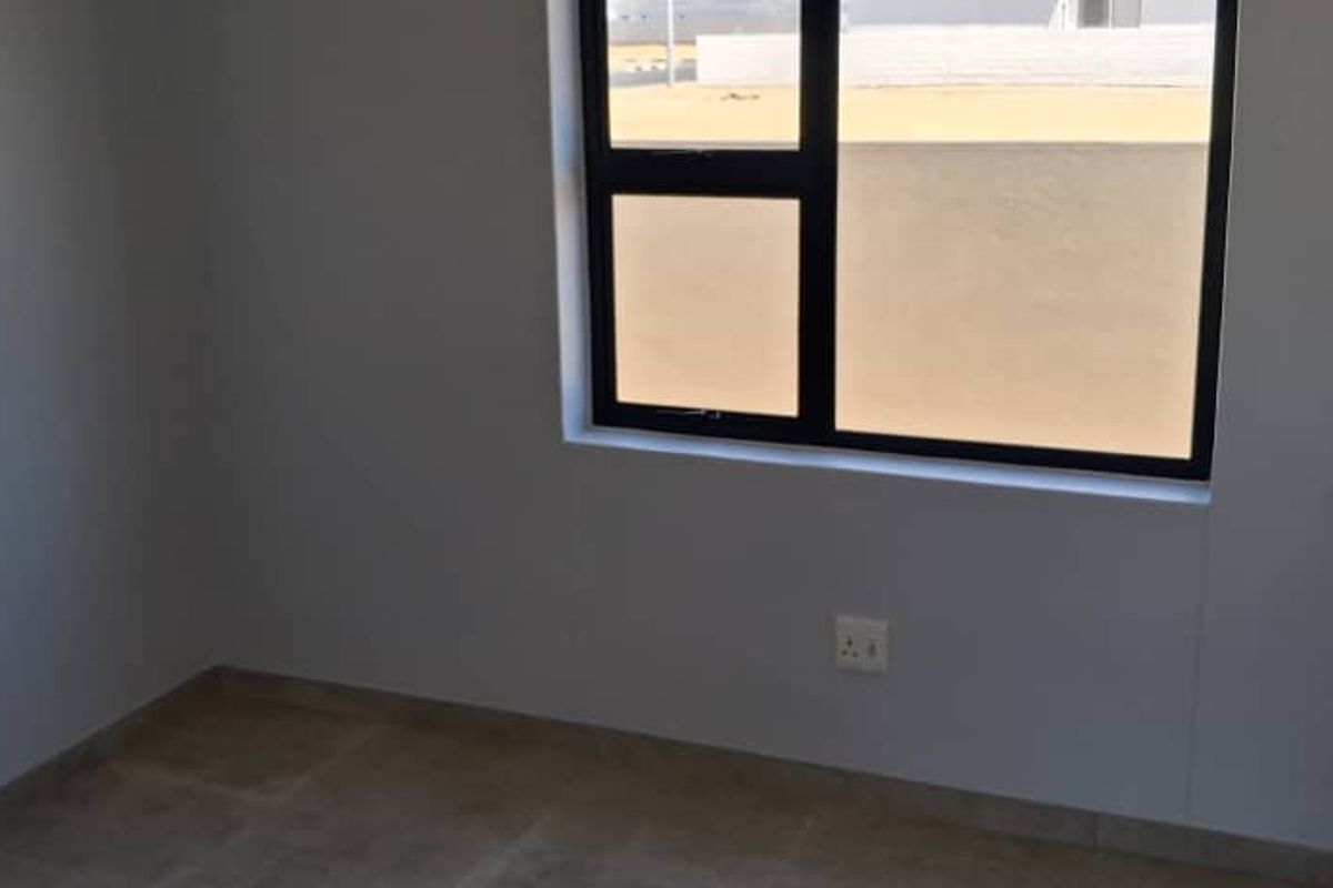 A clean, modern bedroom featuring neutral wall finishes, tiled flooring, and a built-in wardrobe with contemporary handles.
