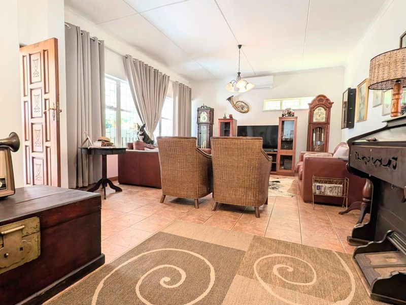 A spacious living room featuring tiled flooring, a split-system air conditioner, and natural light through large windows.