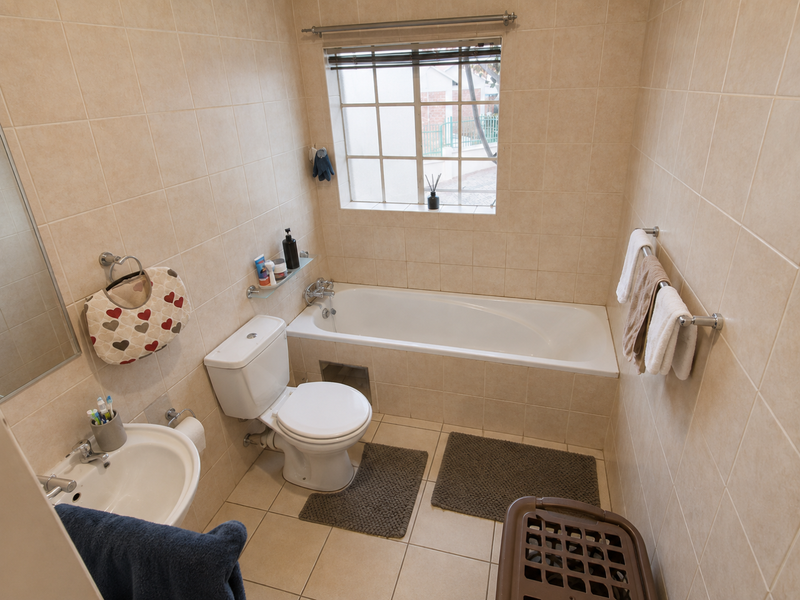 A functional bathroom featuring a bathtub, toilet, and washbasin with neutral wall and floor tiling.
