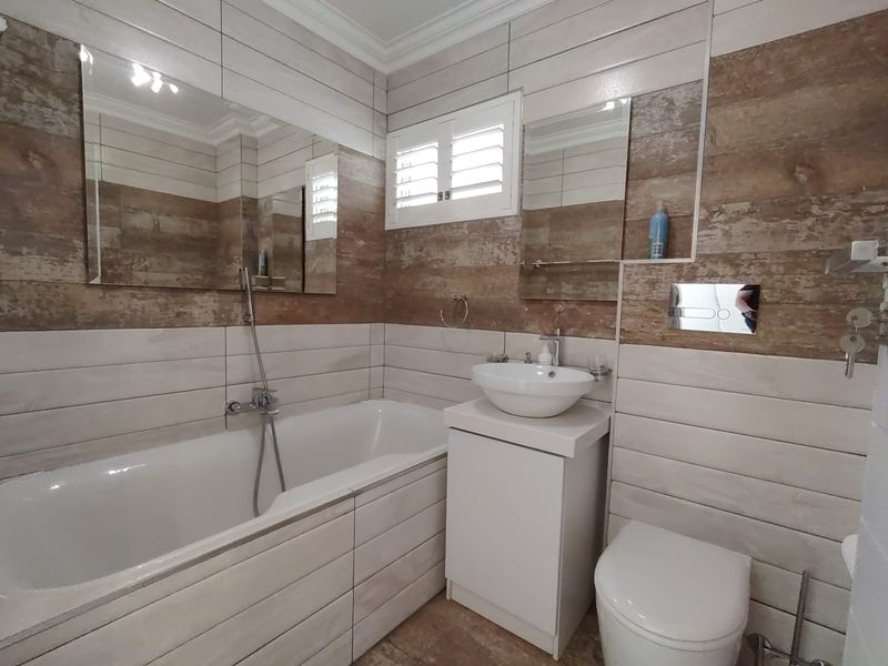 Modern bathroom featuring a bathtub with handheld shower, vessel sink vanity, wall-mounted toilet with concealed cistern, and stylish wood-look tiled walls.