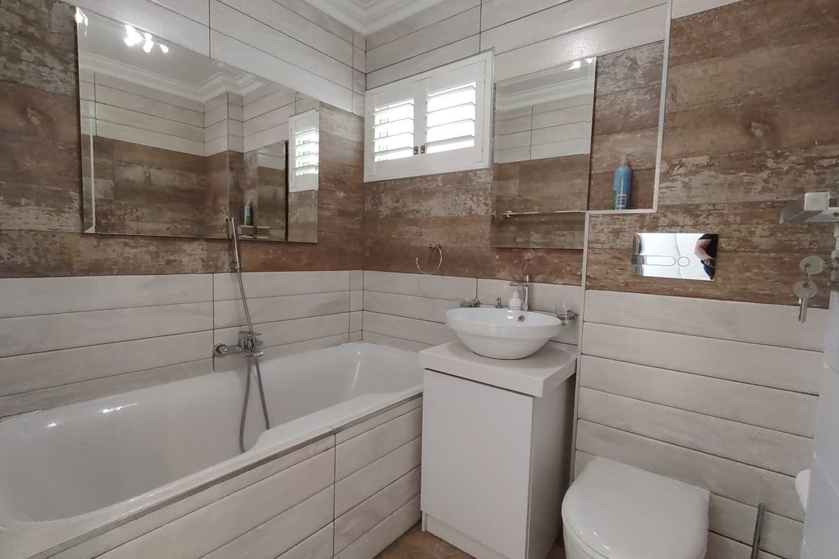 Modern bathroom featuring a bathtub with handheld shower, vessel sink vanity, wall-mounted toilet with concealed cistern, and stylish wood-look tiled walls.